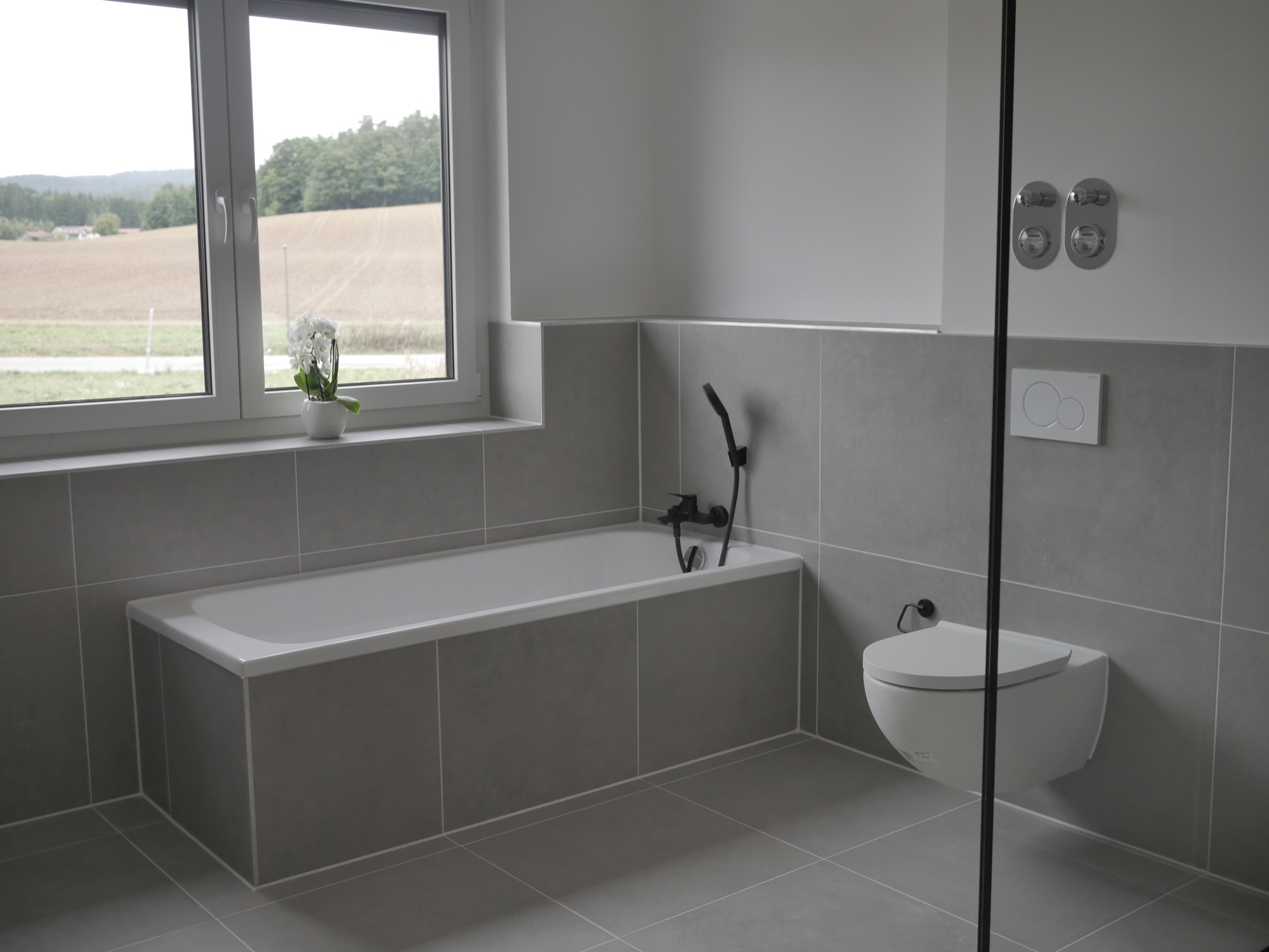 Fertig gefliestes Bad mit verkleideter Badewanne, wandhängendem WC auf Vorwandinstallation und Unterputz-Armaturen